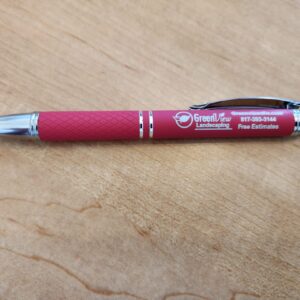 Red ballpoint pen with white text on a wooden surface.