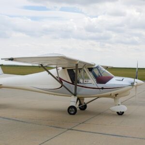 Small white light aircraft parked on a concrete surface under a cloudy sky.