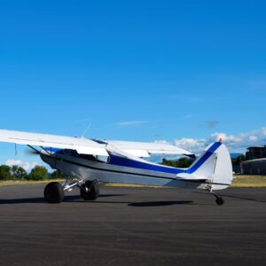 Small single-engine airplane parked on an airstrip under clear blue sky.