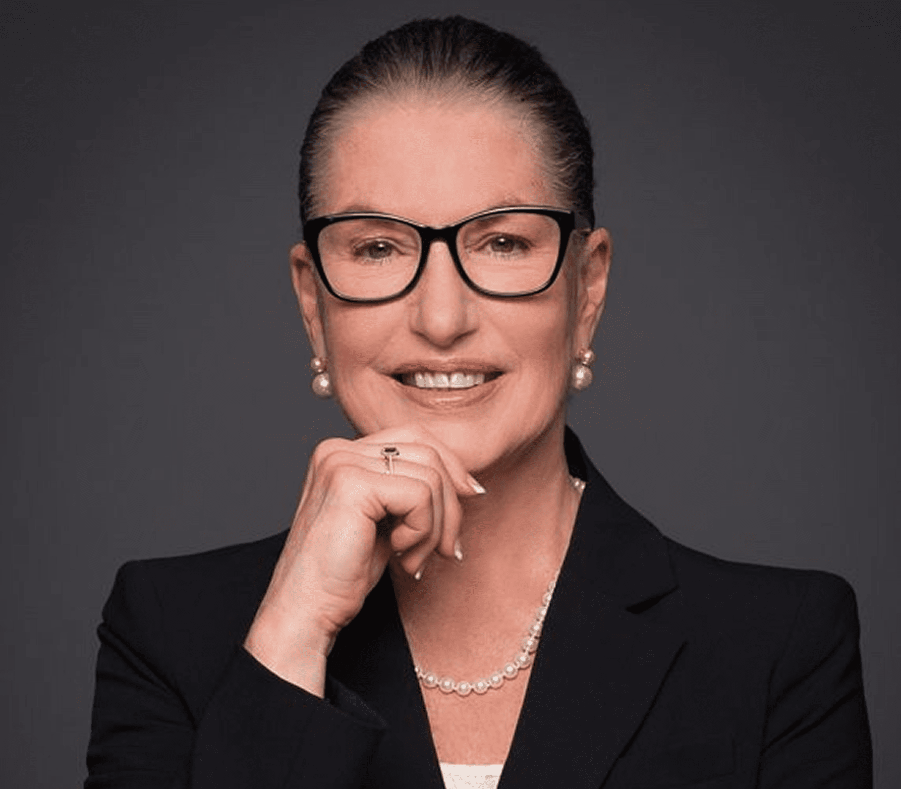 Confident professional woman with glasses and pearl earrings.