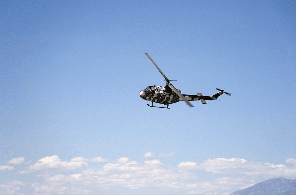 Military helicopter flying in clear blue sky above clouds.