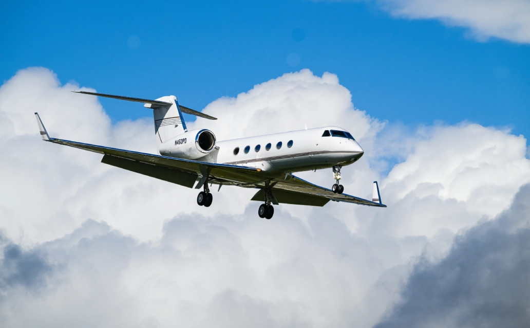 A private jet flying against a blue sky with clouds.