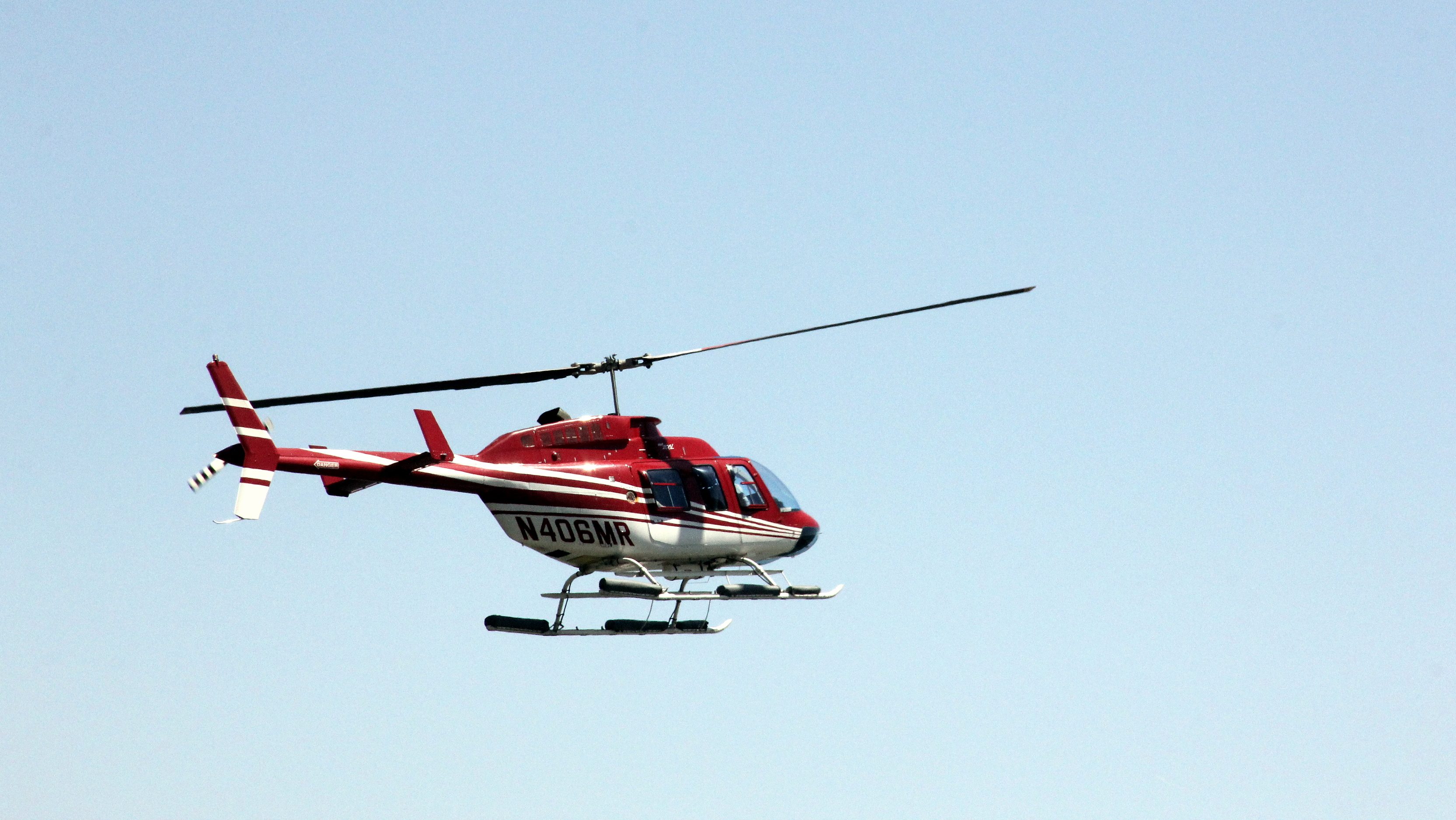 Red and white helicopter flying in clear blue sky.